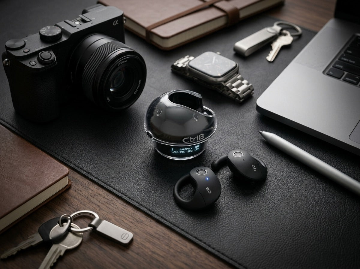 CTRL8 T2 over-the-ear earbuds with UNBLOQ technology placed on a wooden desk alongside a camera and keys